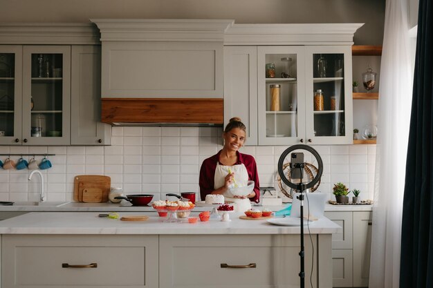 Beautiful young woman preparing cream for homemade cake and recording video for food blog