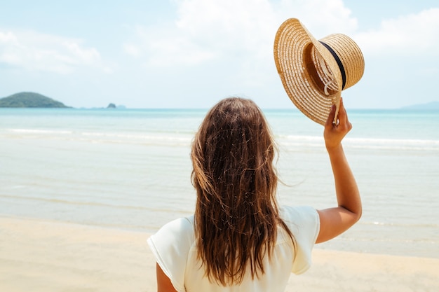 Beautiful young woman raises her hat on a sunny beach