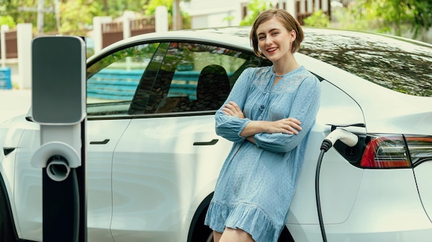 Beautiful young woman recharging her electric car from home EV charging station using alternative energy with net zero emission Modern young girl charging her vehicle before vacation travelPerpetual