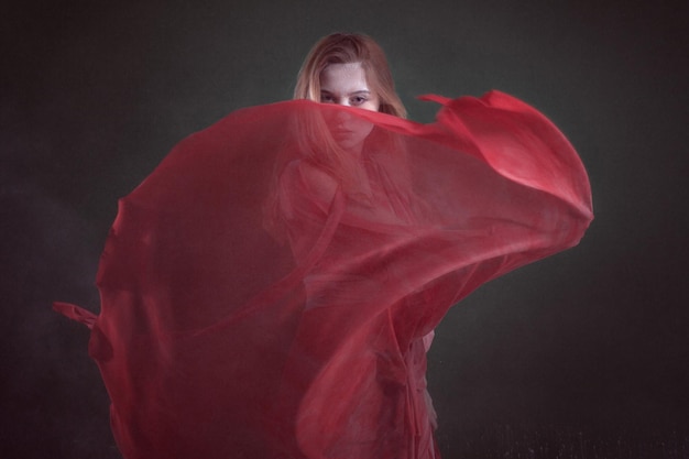 Beautiful young woman in a red dress in a dark room among the flour