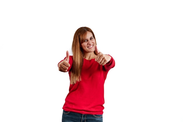 Beautiful young woman in a red sweater, with her thumbs up isolated on a white wall.