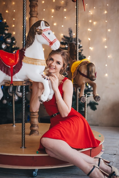 Beautiful young woman rejoices near a carousel with horses. Christmas. 