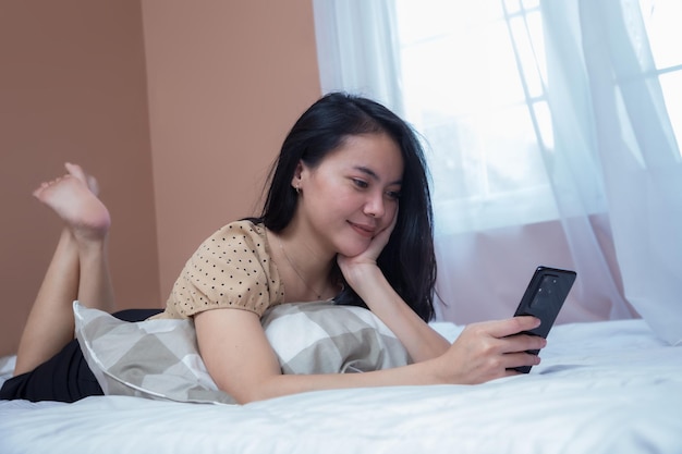 Beautiful young woman relaxing on the bed while holding a cell phone