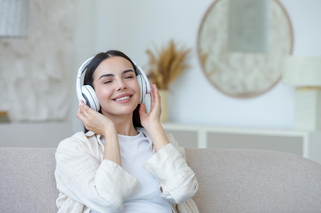 Beautiful young woman resting listening to music in white big headphones brunette sitting on sofa in