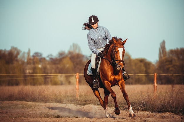 A beautiful young woman riding a horse in a black helmet and boots