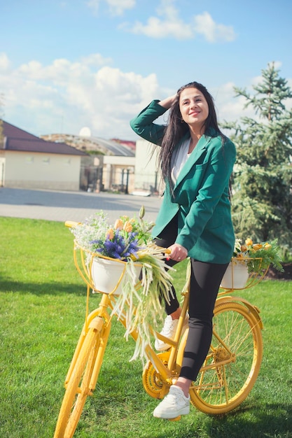 Beautiful young woman riding a yellow bike with flowers basket