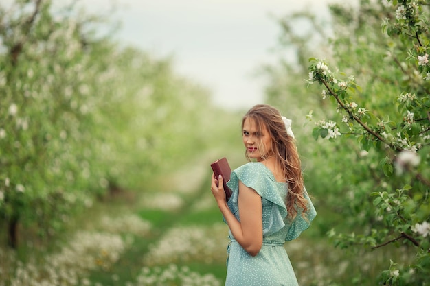 Beautiful young woman in a romantic dress reads a second book in spring in a blooming garden