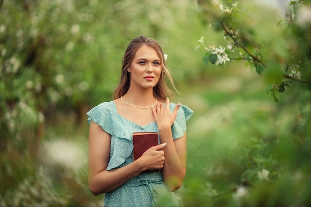 Beautiful young woman in a romantic dress reads a second book in spring in a blooming garden