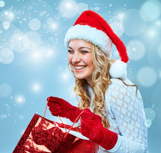 Beautiful young woman in Santa Claus clothes with a gift on a blue background