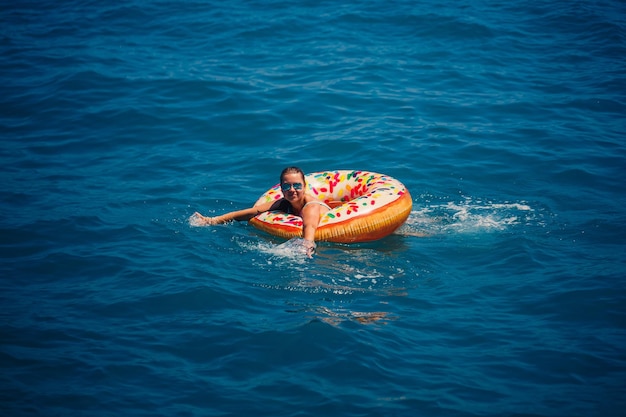 Beautiful young woman in the sea swims on an inflatable ring and has fun on vacation Girl in a bright swimsuit at the sea under the sunlight