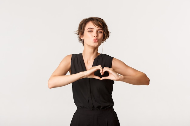 Beautiful young woman sending air kiss and showing heart gesture