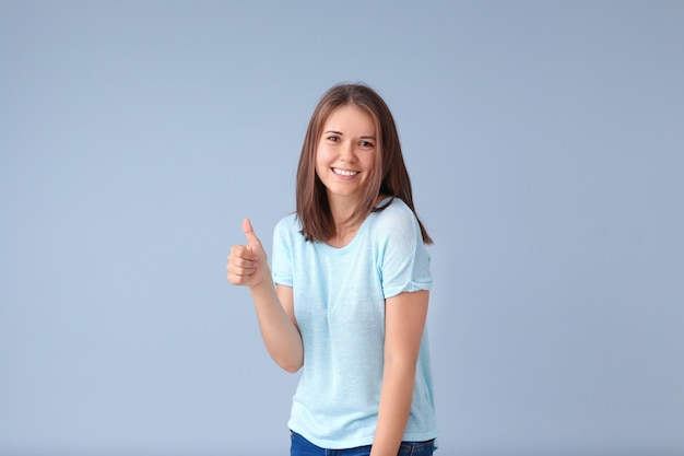 Beautiful young woman showing thumb-up gesture on blue