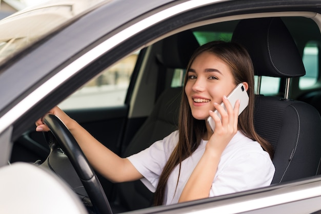 Beautiful young woman sitting in the car with laptop and talking on phone.