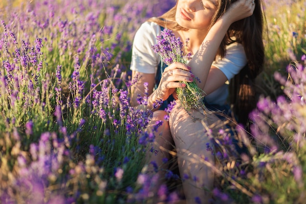 Beautiful young woman sitting in a meadow with a bouquet of lavender and dreaming in the sunset rays