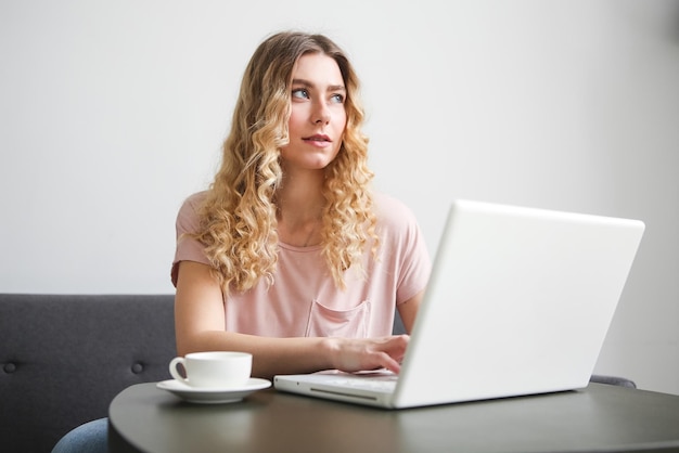 Beautiful young woman sitting on the sofa with white cup of coffee working on white laptop Girl in