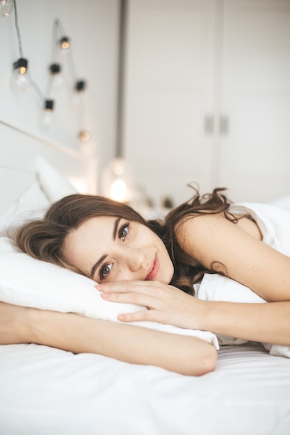 Beautiful young woman sleeping in comfortable bed on white fresh sheets. Female person wake up in the morning, eyes open. Healthy sleep concept.