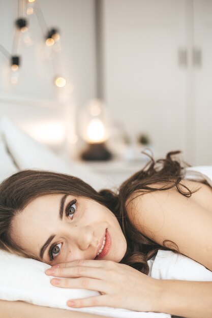 Beautiful young woman sleeping in comfortable bed on white fresh sheets. Female person wake up in the morning, eyes open. Healthy sleep concept.