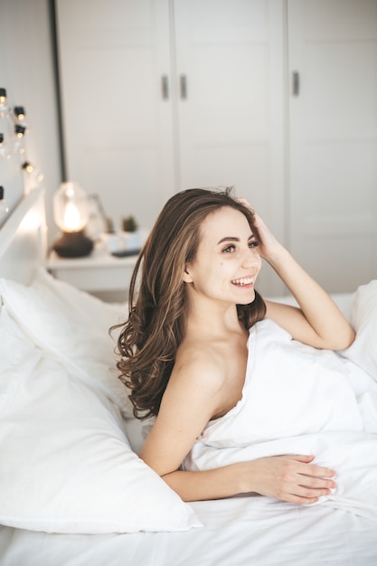 Beautiful young woman sleeping in comfortable bed on white fresh sheets. Female person wake up in the morning, eyes open. Healthy sleep concept.