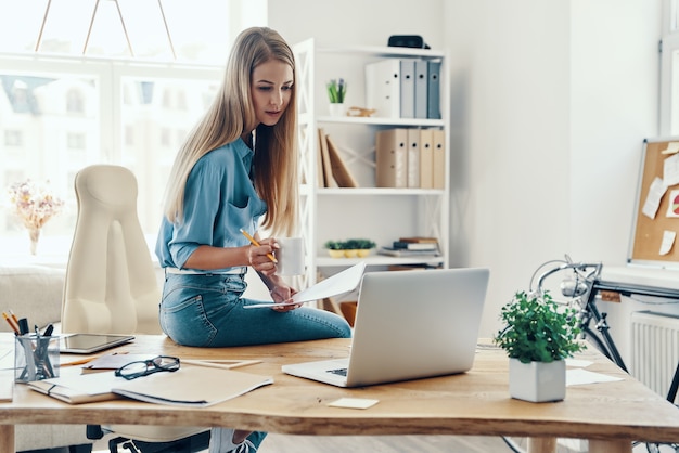 Beautiful young woman in smart casual wear using laptop while working in the office