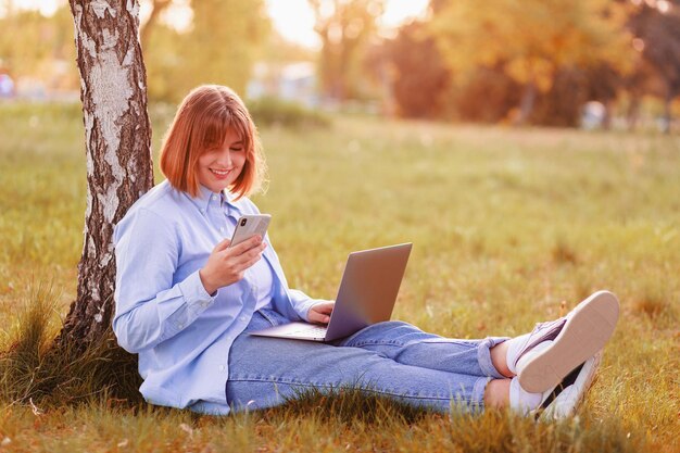 beautiful young woman smiling with her teeth sitting in a green park and working on a laptop