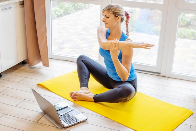 Beautiful young woman in sportswear doing sport exercises on yoga mat at home