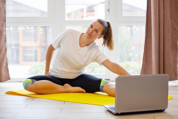 Beautiful young woman in sportswear doing sport exercises on yoga mat at home