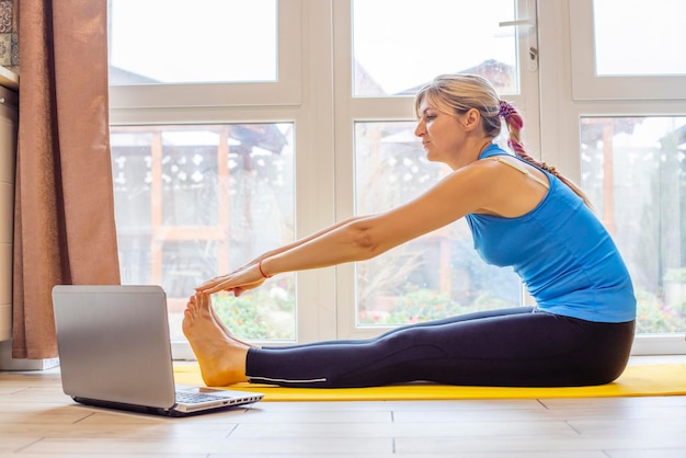 Beautiful young woman in sportswear doing sport exercises on yoga mat at home