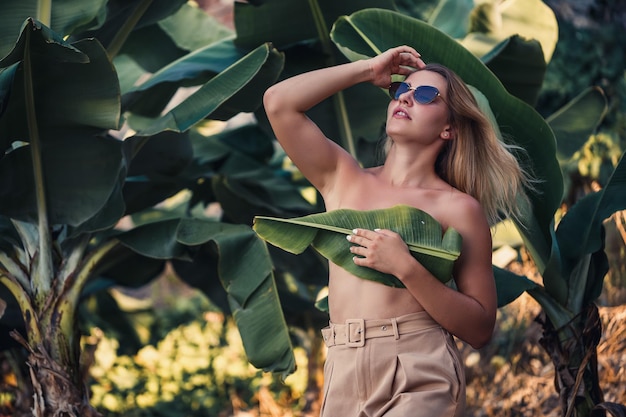 Beautiful young woman stands in a beautiful pose near a banana tree portrait shooting on a banana plantation