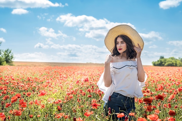 Beautiful young  woman in a straw hat in a poppy field at summertime