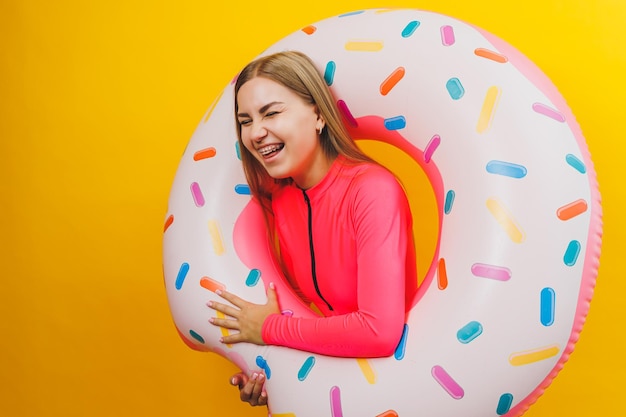 Beautiful young woman in a stylish pink swimsuit with a donut inflatable ring on a yellow background