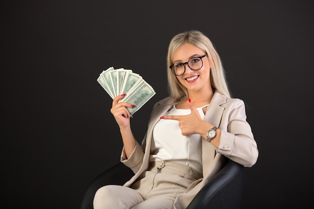 beautiful young woman in a suit on black with dollars in hands