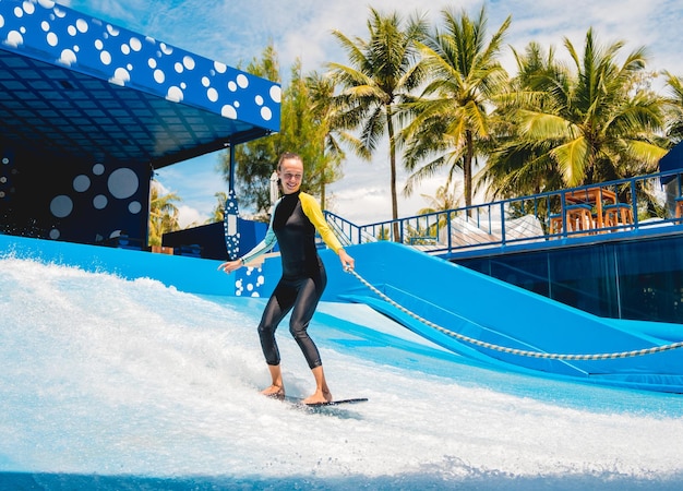 Beautiful young woman surfing with trainer on a wave simulator at a water amusement park