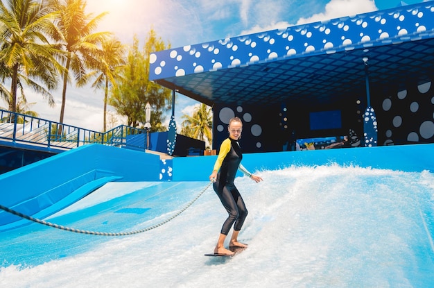 Beautiful young woman surfing with trainer on a wave simulator at a water amusement park