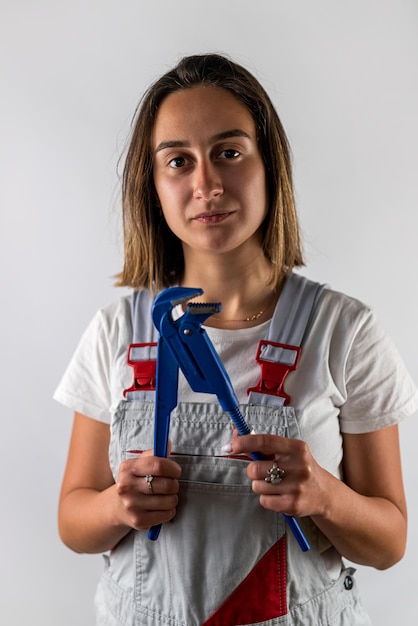 Beautiful young woman in suspenders holds a blue wrench in her hands