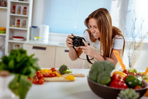 Beautiful young woman taking photo of healthy salad with digital photo camera for her blog.