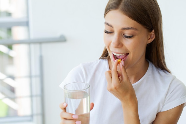 Beautiful Young Woman Taking Yellow Fish Oil Pill