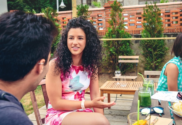 Beautiful young woman talking with a friend around the table with healthy drinks in a leisure summer day outdoors