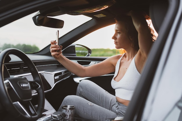 Beautiful young woman travel on the roads by car stopped at the side of the road photographs on a smartphone