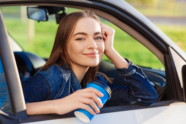 Beautiful young woman traveled on road in car drinking coffee from disposable