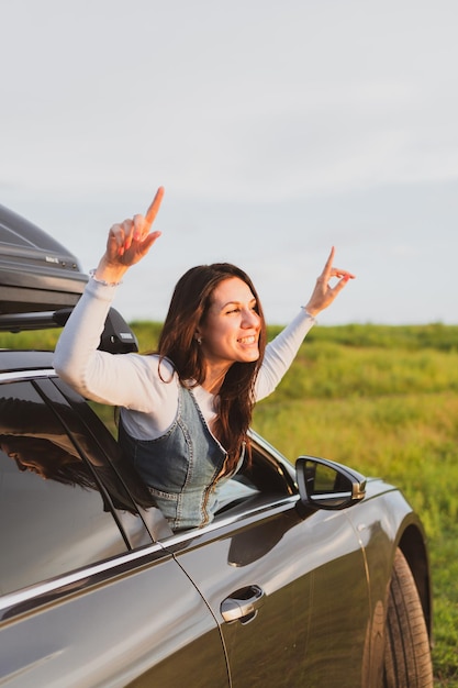 Beautiful young woman travels by car leaning out the window and having fun