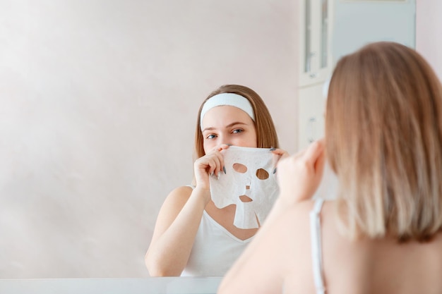 Beautiful young woman use sheet facial mask on face skin for beauty spa skincare at home bathroom