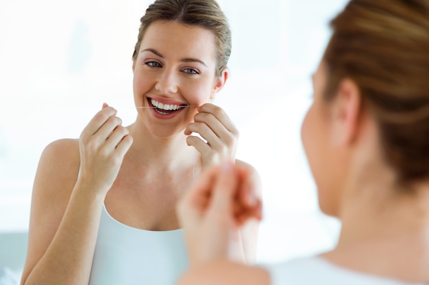 Beautiful young woman using dental floss in a home bathroom.