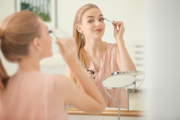 Beautiful young woman using eyelash brush at home