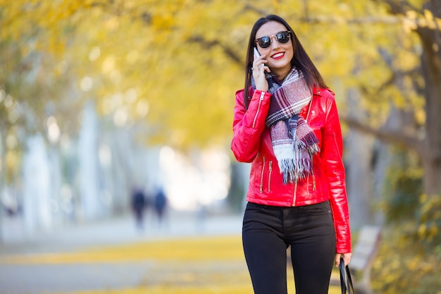 Beautiful young woman using her mobile phone in autumn.