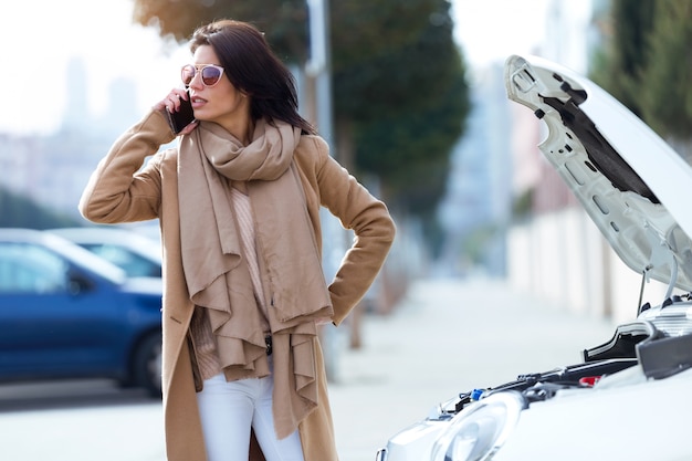 Beautiful young woman using her mobile phone calls for assistance for car.