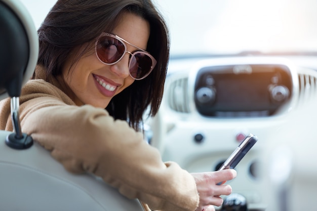 Beautiful young woman using her mobile phone in the car.