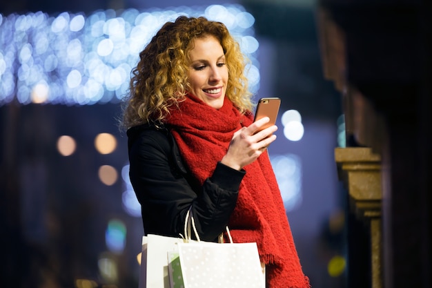 Beautiful young woman using her mobile phone in the street at night.