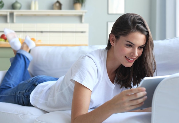 Beautiful young woman using tablet sitting on sofa at home at living room