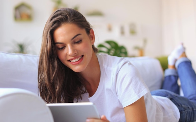 Beautiful young woman using tablet sitting on sofa at home at living room