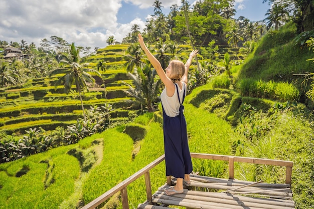 Beautiful young woman walk at typical Asian hillside with rice farming mountain shape green cascade rice field terraces paddies Ubud Bali Indonesia Bali travel concept